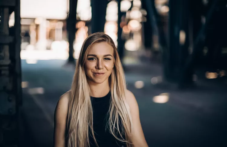 Laura auf dem Industriegelände. Sie trägt ein schwarzes Schulterfreies Kleid